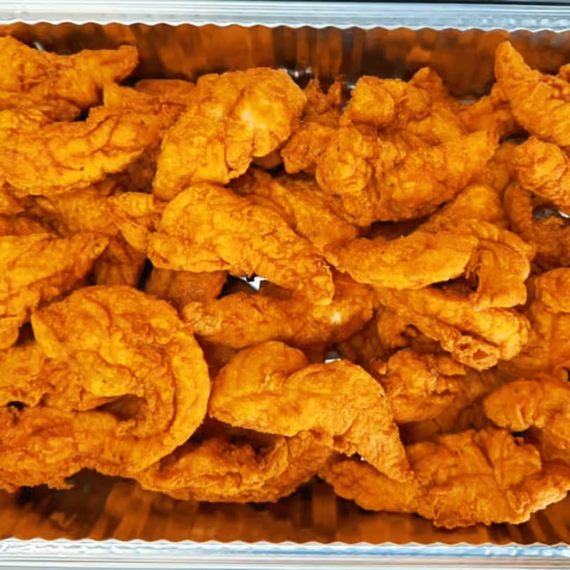 Close-up of a catering tray filled with golden-brown fried chicken pieces, ready to serve.