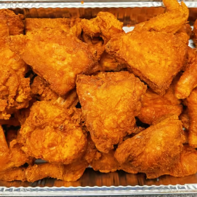 Close-up of crispy, golden-brown fried chicken pieces in a silver foil tray.