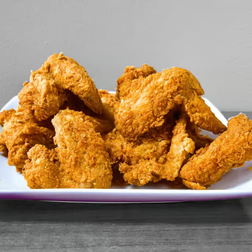 A large platter of golden-brown fried chicken pieces on a white plate.